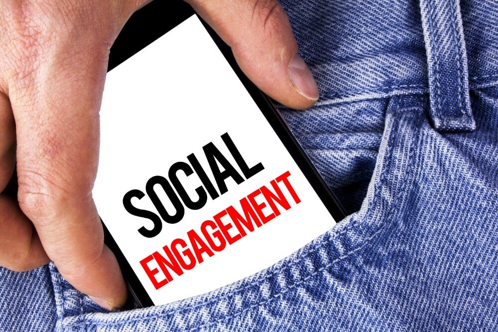 Hand haalt smartphone met tekst 'Social Engagement' uit spijkerbroekzak